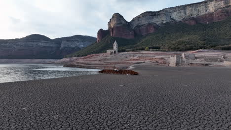 shipwreck of boat on dry shores of sau marsh with church ruin in background, catalonia, spain