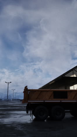 a yellow dump truck parked in a parking lot with a city in the background