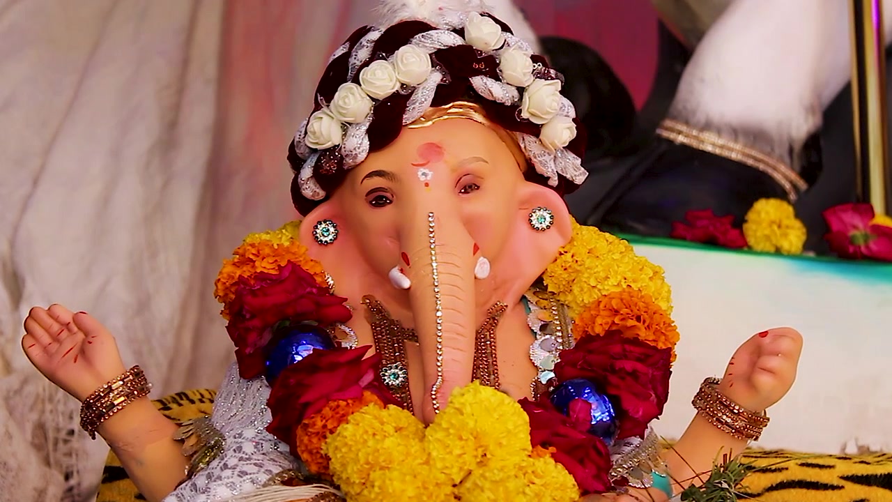 Primo piano dell'idolo di Ganesha con turbante di rose, mani sollevate in posa benedicente con ghirlanda di calendule, festival di Ganesh Chaturthi in India
