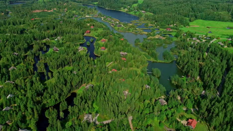 Paisaje-Verde-Con-Pequeñas-Casas-Aisladas-Inmersas-En-La-Exuberante-Naturaleza-De-Bosques-Y-Lagos,-Vista-Aérea-De-Drones-De-Retorno