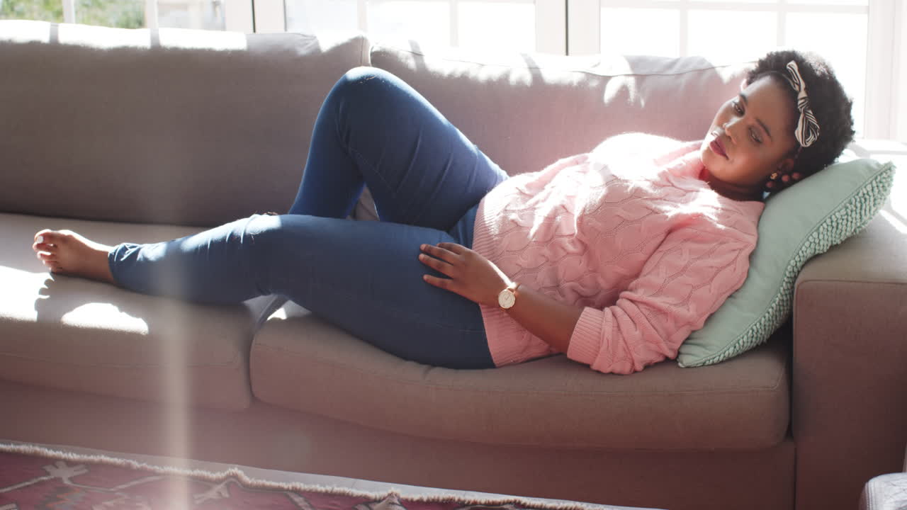 African American woman rests on a couch at home, sunlight streaming in