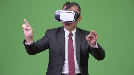 mature japanese businessman using virtual reality headset against green background