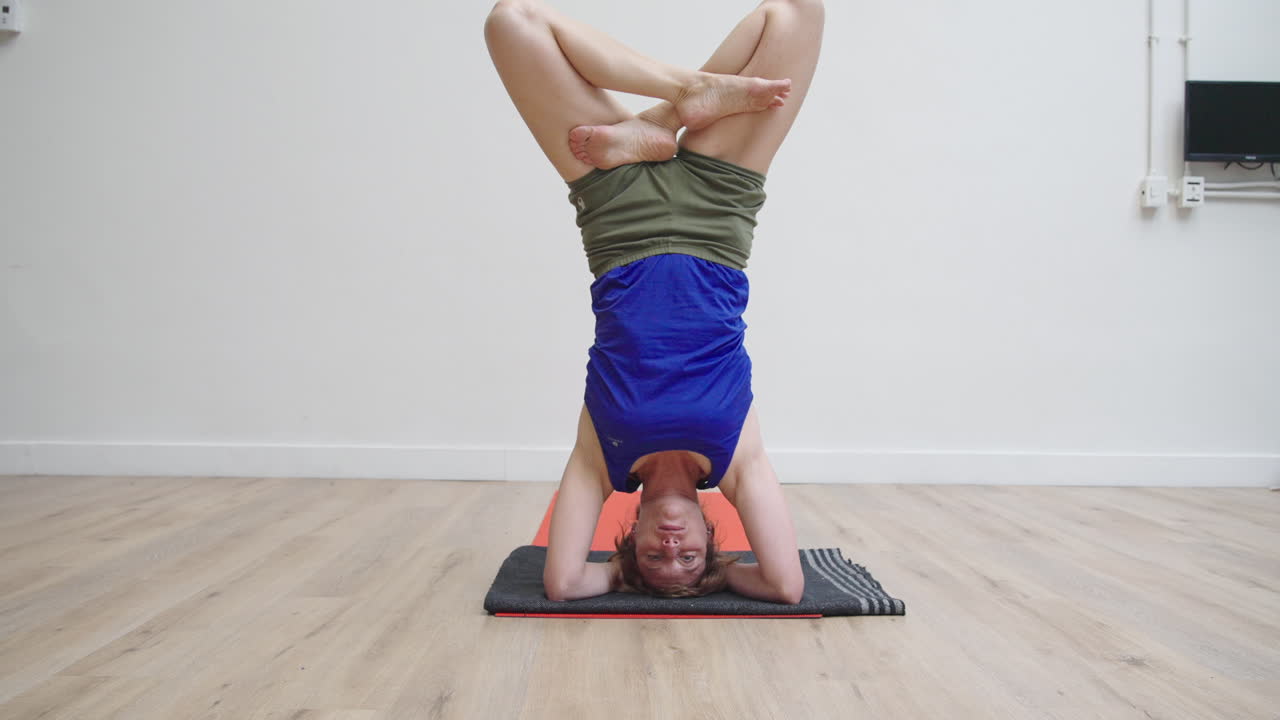 Mulher fazendo invertida sobre a cabeça de yoga com pernas cruzadas.