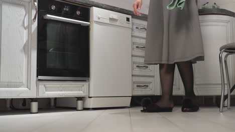 leg view of female chef wearing transparent long hose under flowing gown and flat slippers as she dances gracefully in kitchen, showing playful footwork near oven, chair, and kitchen cabinet
