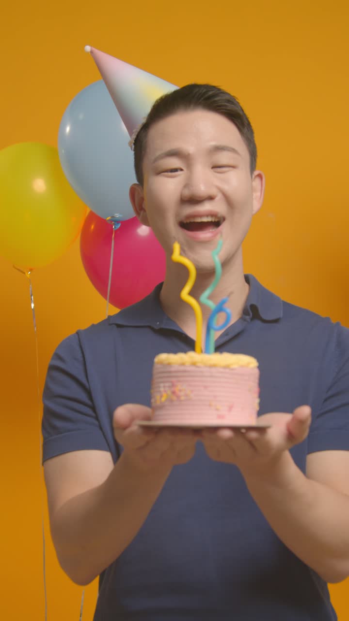 retrato vertical de estudio de video de un hombre con sombrero de fiesta celebrando su cumpleaños soplando velas en el pastel