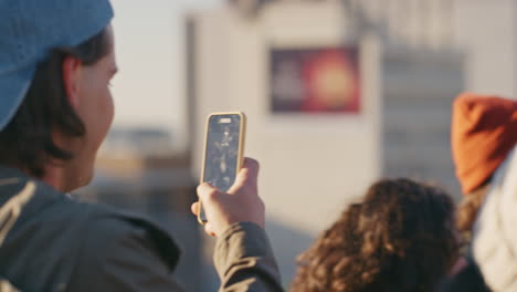 Fröhliche-Gruppe-Von-Freunden,-Die-Auf-Dem-Dach-Feiern.-Junger-Mann-Nutzt-Smartphone,-Fotografiert-Feierwochenende-Und-Genießt-Den-Sonnenuntergang-Mit-Seiner-Freundin