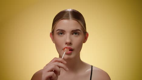 retrato de una hermosa mujer joven lamiendo una sabrosa piruleta dulce, fondo amarillo