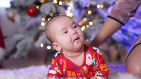 mommy's helping her little son to lie down comfortably on a fluffy plaid. tiny kid looking up at his caring mother. blurred backdrop with christmas tree.