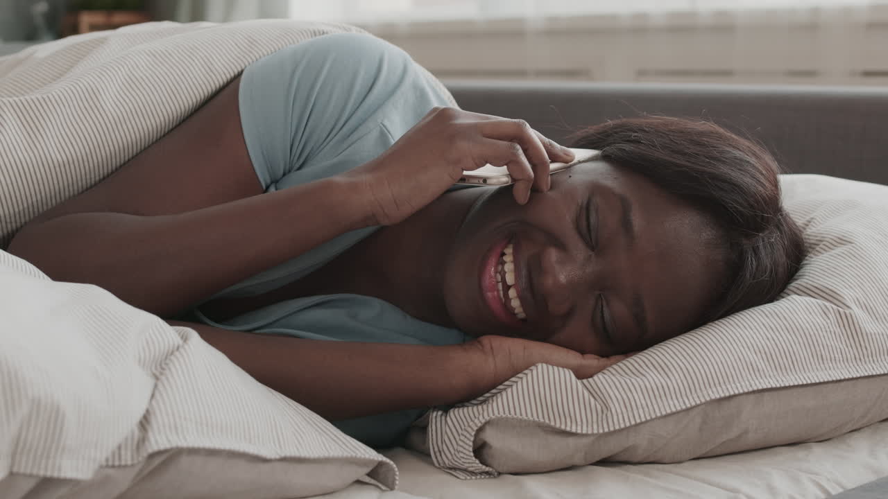 Afrikansk kvinde ligger i sengen og taler i telefon