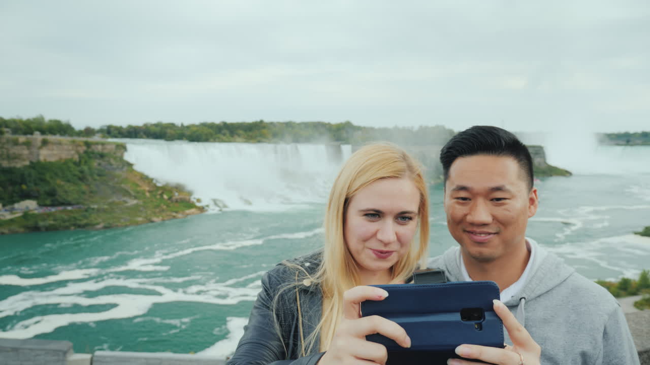 una joven pareja multiétnica admira una hermosa vista de las cataratas del niágara en américa y cana