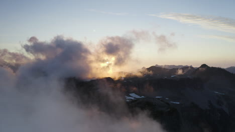 Drohne-Steigt-Zwischen-Dicker-Wolkendecke-Auf,-Während-Sonnenlicht-Vom-Sonnenuntergang-Zwischen-Wolken-Vor-Blauem-Himmel-In-Den-Bergen-Des-Pazifischen-Nordwestens-Diffundiert