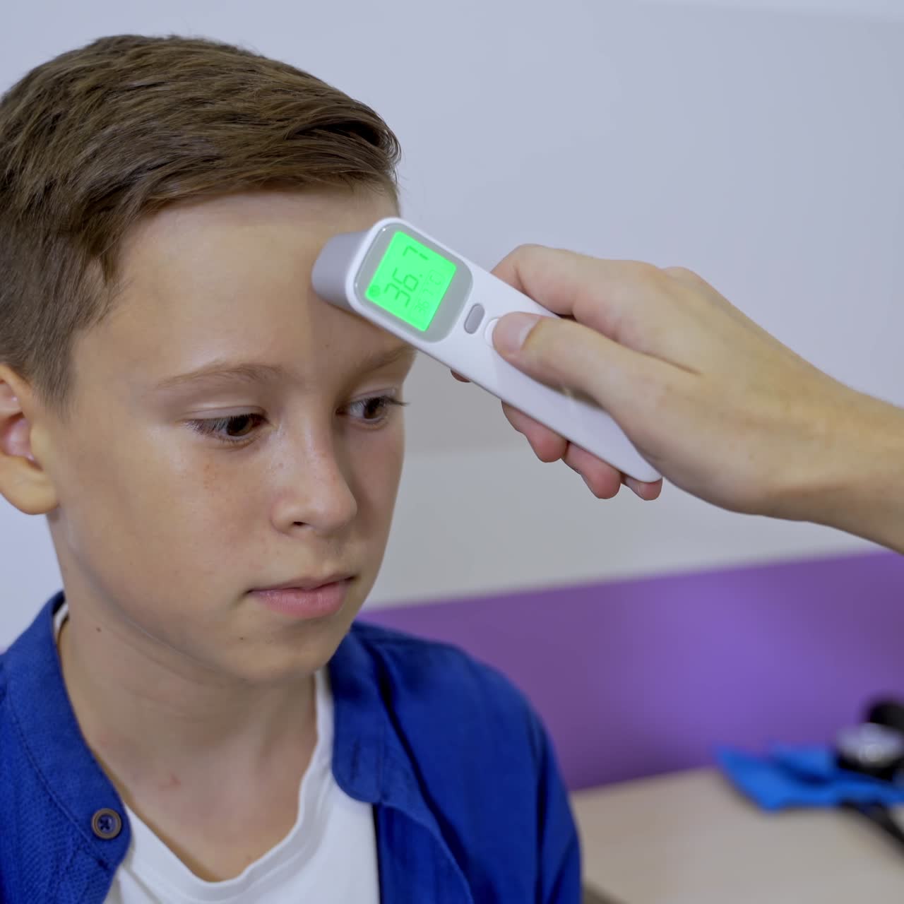 Pediatrician or doctor checks boy`s body temperature using infrared forehead thermometer. Teenager at doctor`s cabinet. Selective focus
