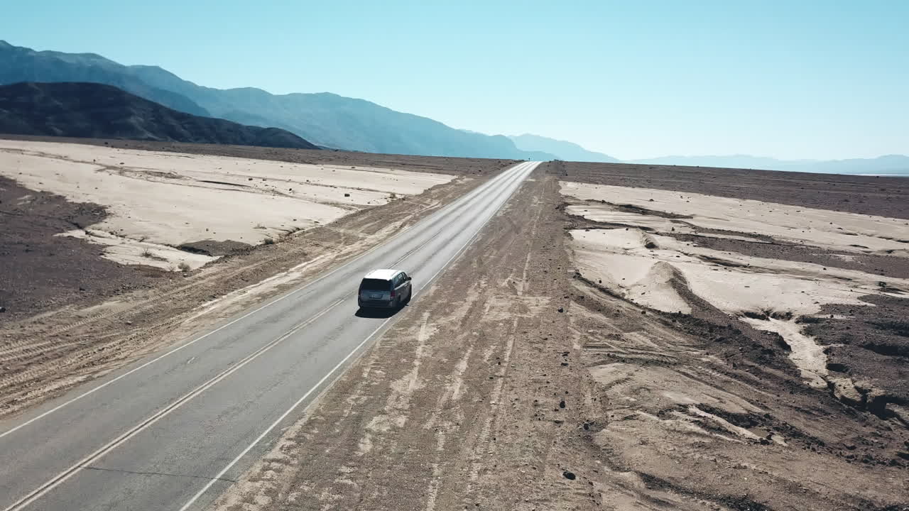 Toma aérea de seguimiento de un coche circulando por un paisaje desértico en el Parque Nacional del Valle de la Muerte, California