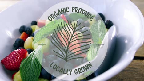 animation of organic produce locally grown text banner over bowl of fruit salad on wooden table