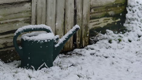 Short-time-lapse-of-snow-building-up-over-an-old-watering-can-in-a-front-of-a-shed,-in-a-traditional-english-garden