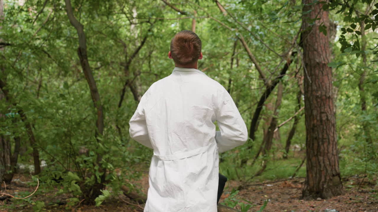 Back view of scientific researcher in white shirt wearing white coat in forest surrounded by lush greenery and tall trees, highlighting outdoor scientific preparation, exploration