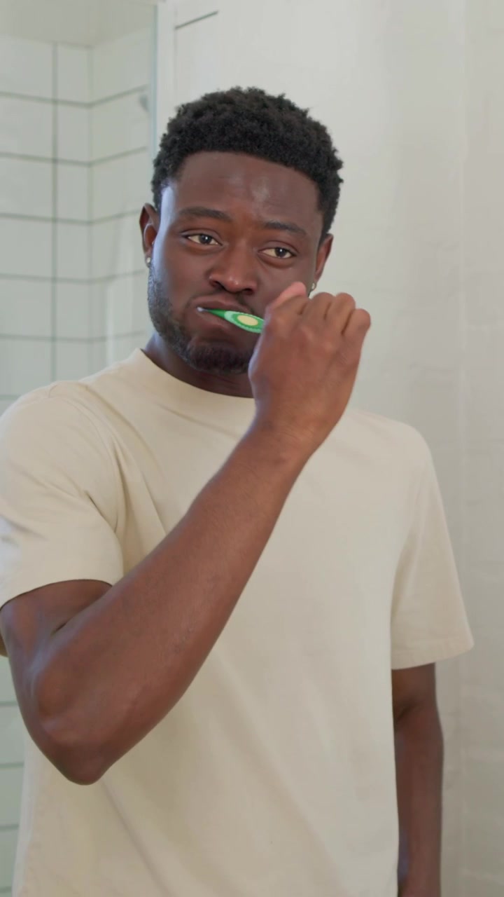 Vertical video: Picking up green brush and paste, man wetting brush and brushing teeth at home sink
