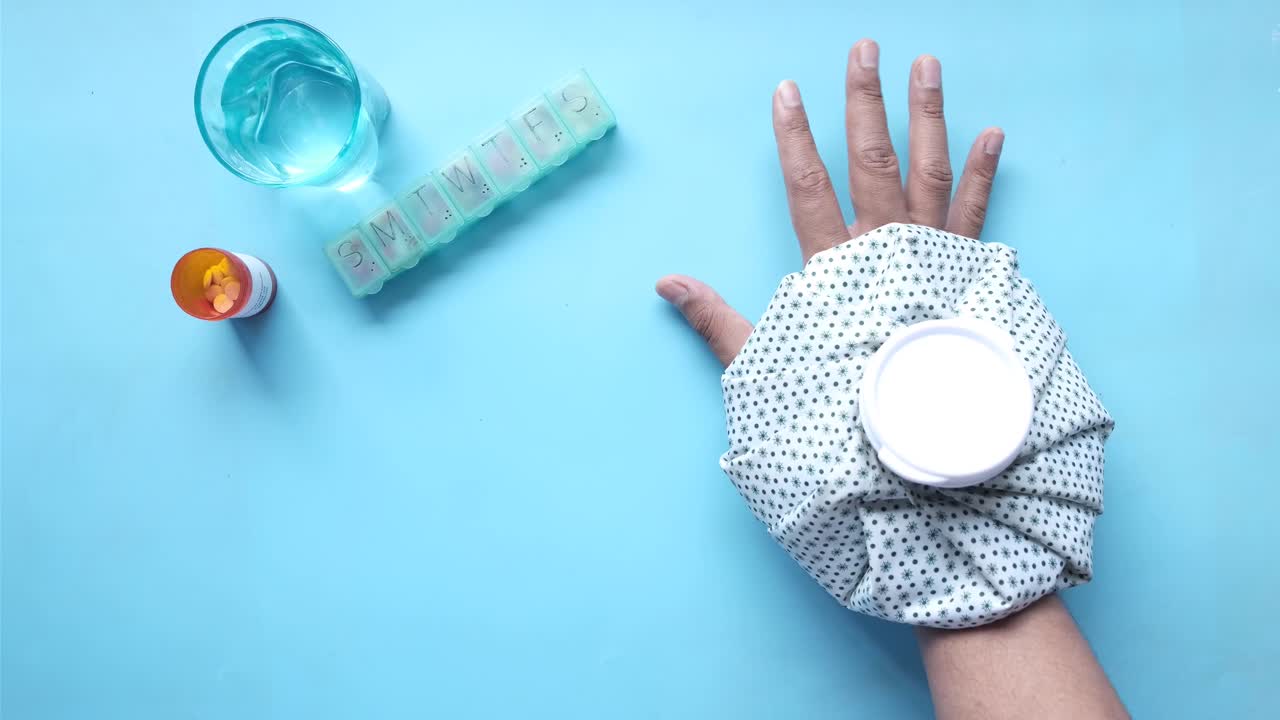 mano herida con una bolsa de hielo y medicamentos