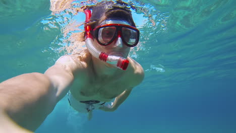 entusiasta buzo masculino con snorkel rojo nadando en agua de mar azul, observando la vida submarina y el fondo marino en slowmo