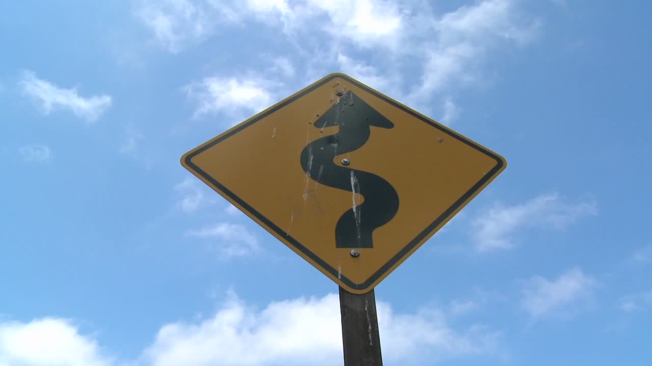 lapso de tiempo de las nubes moviéndose sobre una señal de tráfico advirtiendo de las curvas por delante