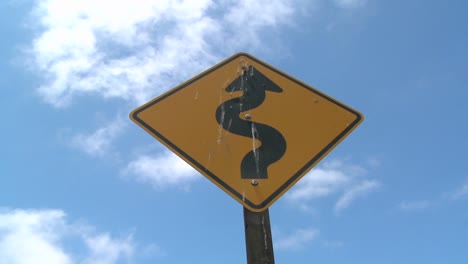 time lapse of clouds moving over a road sign warning of curves ahead