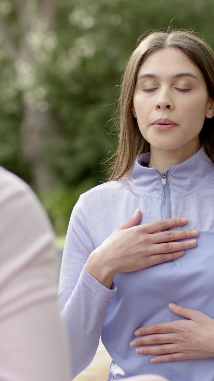 Video vertical: Mujer con top morado colocando las manos en el pecho y el vientre, respirando en el parque, con un reloj inteligente