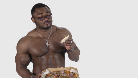 black man enjoys eating pizza. portrait of a muscle sportsman with black skin eats tasty pizza on white studio background. unhealthy food.