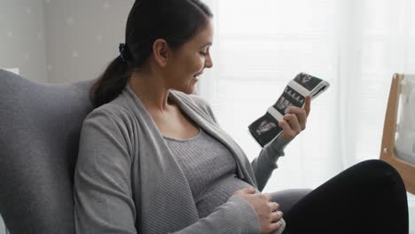 Close-up-video-of-caucasian-woman-in-advanced-pregnancy-browsing-ultrasound-scan-in-baby's-room.