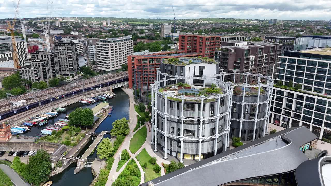 Aerial pan of Coal Drops Yard, London, featuring passing train, canal-side luxury and iconic Gas Holder apartments amid landscaped urban regeneration in the heart of King’s Cross.