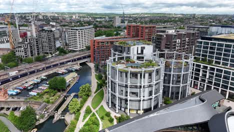 aerial pan of coal drops yard, london, featuring passing train, canal-side luxury and iconic gas holder apartments amid landscaped urban regeneration in the heart of king’s cross.