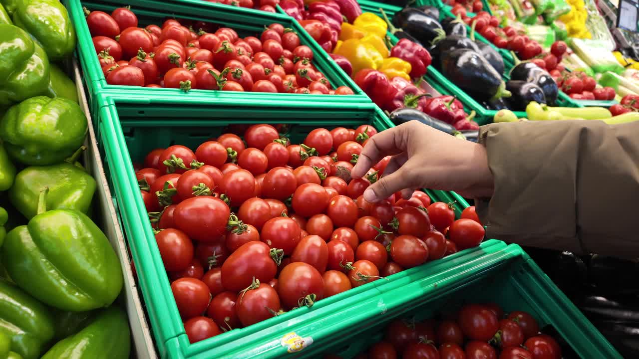 Hand selecting ripe tomatoes in a supermarket produce aisle