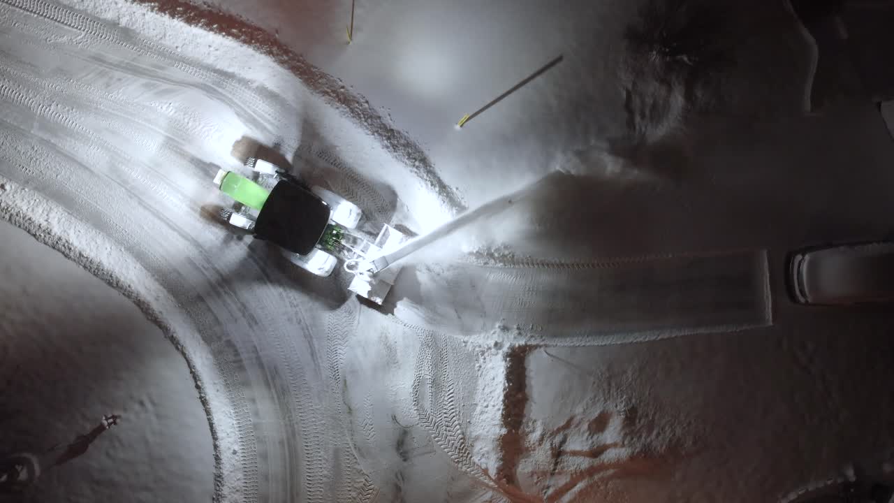 Birdseye Aerial View of Snowblower Removing Snow From Driveway and Street at Night, High Angle Drone Shot