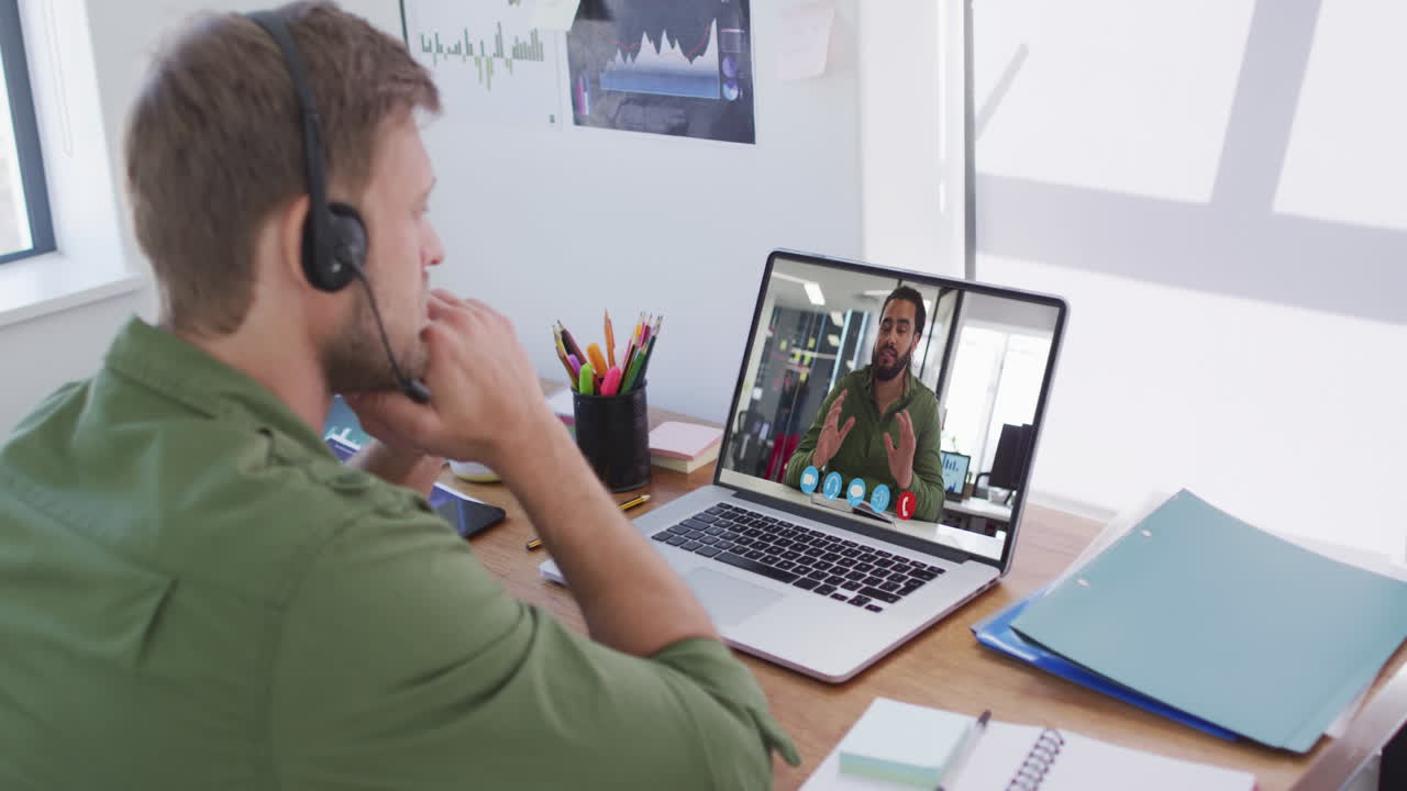 Kaukasisk mand med telefonheadset på har videoopkald med mandlig kollega på bærbar computer på kontoret