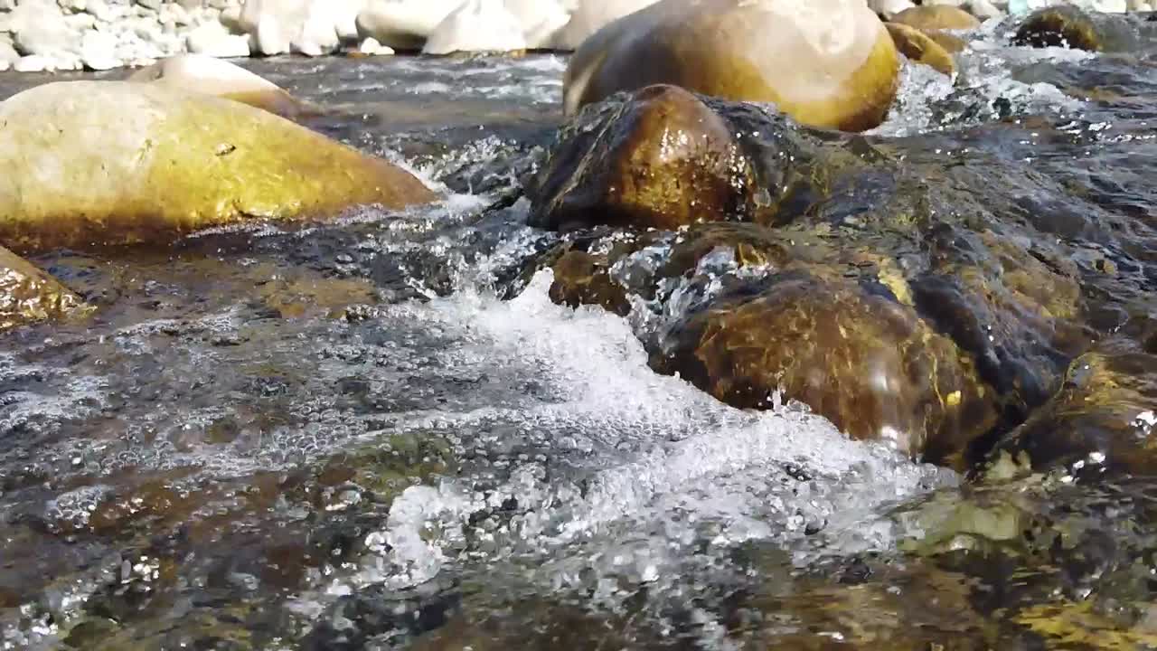 Primo piano al rallentatore di acqua fresca che scorre sulle rocce. Il ruscello limpido mette in risalto la natura preziosa delle risorse idriche nei Monti Atlas del Marocco, soggetti alla siccità.