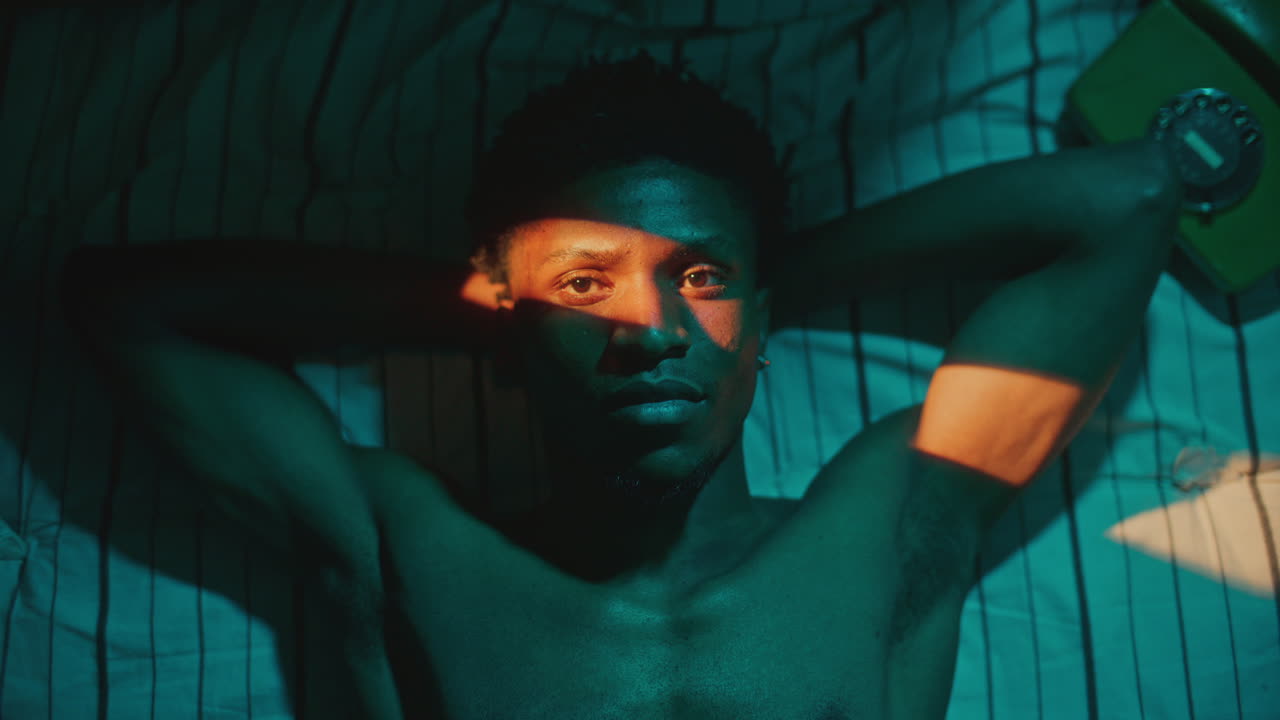 Portrait of Young Black Man Lying on Bed Illuminated by Streak of Light