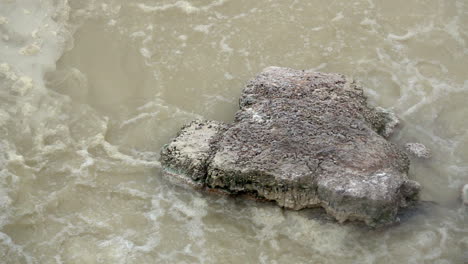 slow motion shot of boiling water surrounding a rock in a geothermal hot spring