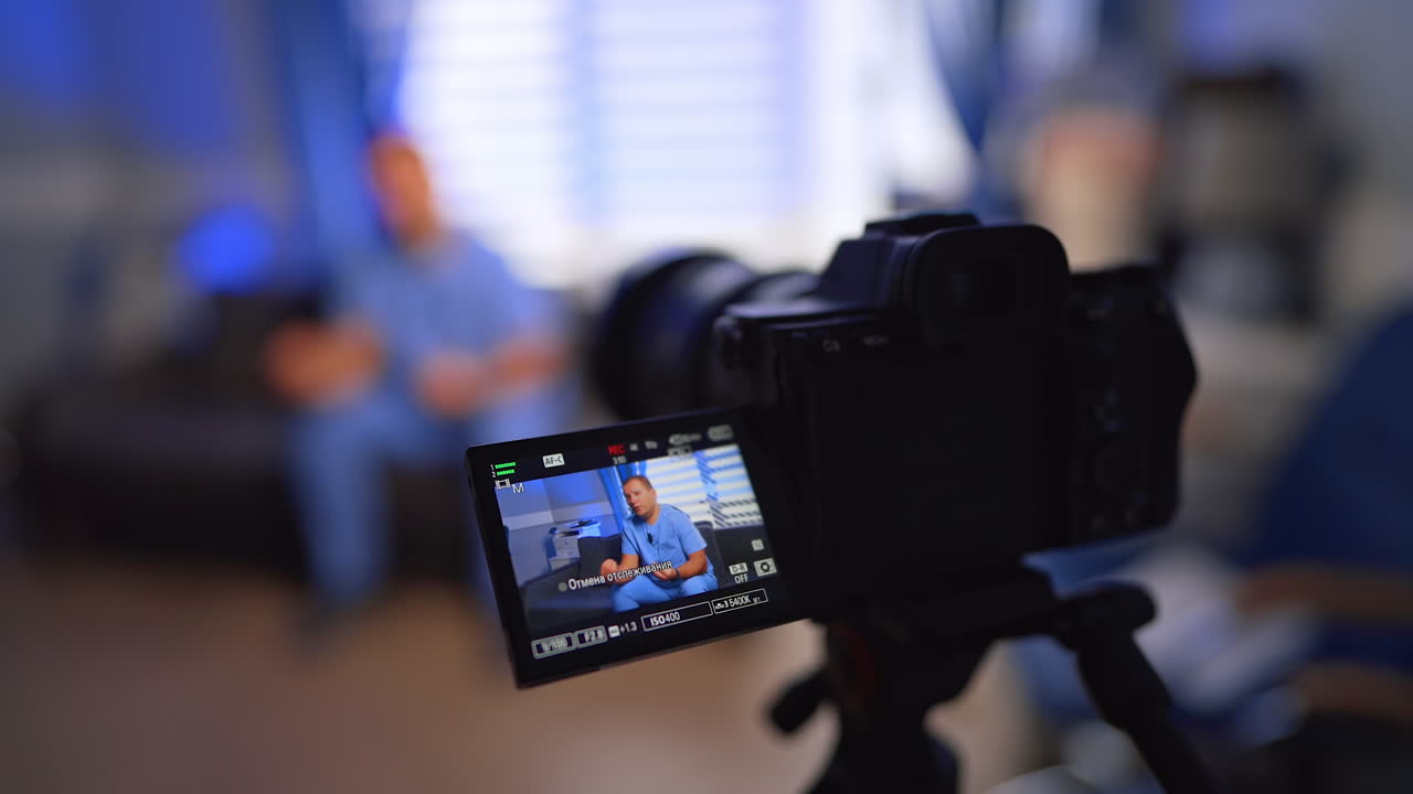 Modern camera recording a medical vlog. Close up. Man in blue uniform sits on sofa speaking for the video. Selective focus