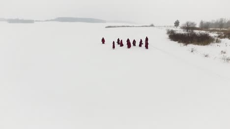 personas con túnicas rojas caminando a través de un paisaje nevado