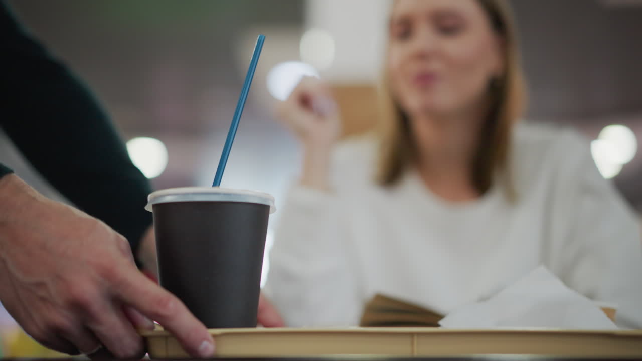 여성의 클로즈업은 배경에서 흐릿하게 열려있는 책을 읽고, 전면에 트레이에 제공되는 아침 식사는 부드러운 조명과 활기찬 보케를 가진 현대적인 레스토랑 설정입니다.