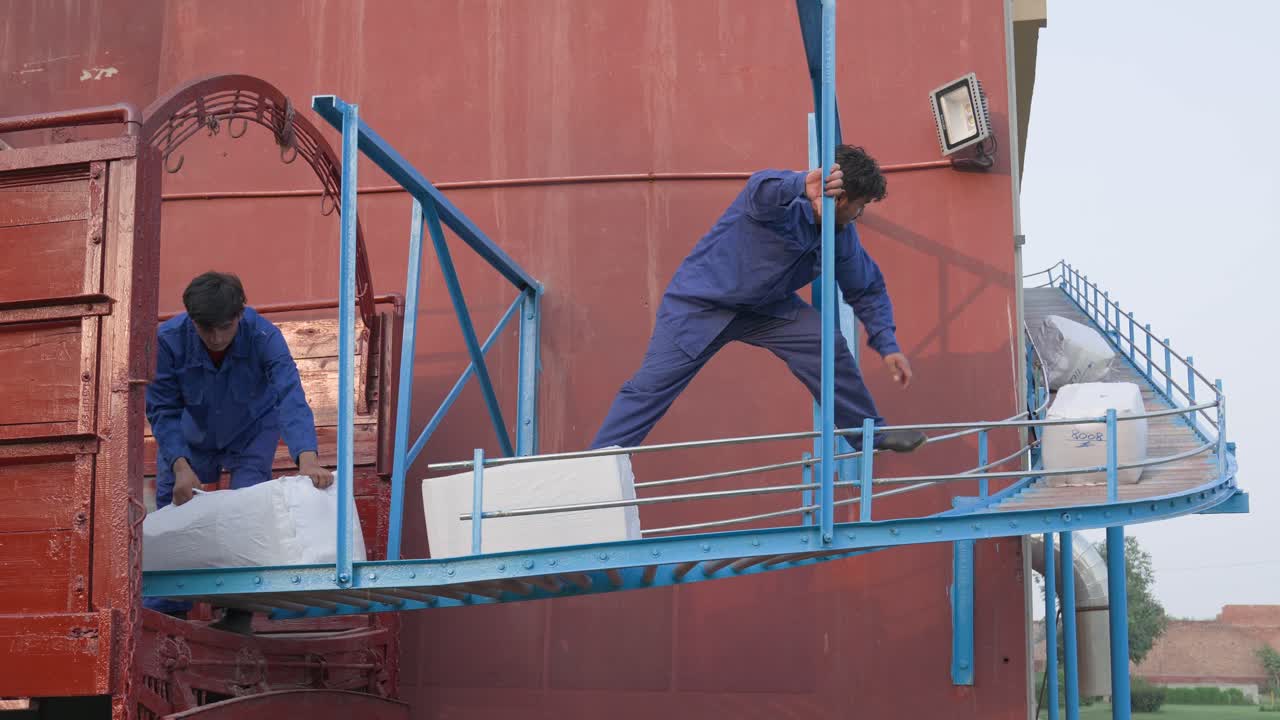 Packages Travelling Down A Outdoor Conveyor Belt And Workers Loading Them Into A Truck For Shipping.