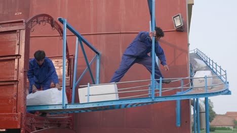 packages travelling down a outdoor conveyor belt and workers loading them into a truck for shipping.