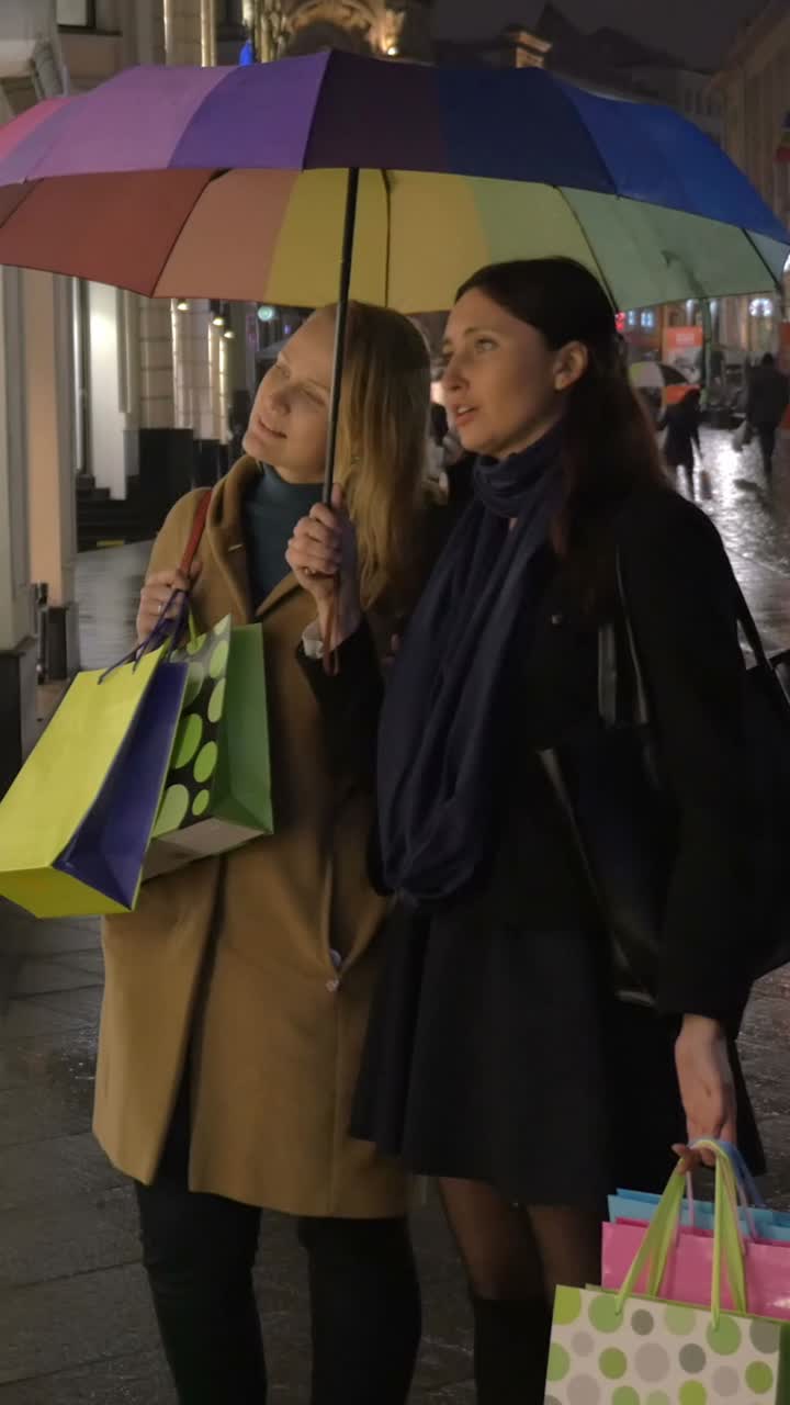 Women with Shopping Bags Under Umbrella on City Street