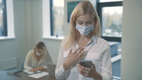 business woman with face mask having a business video call holding a smartphone in the office