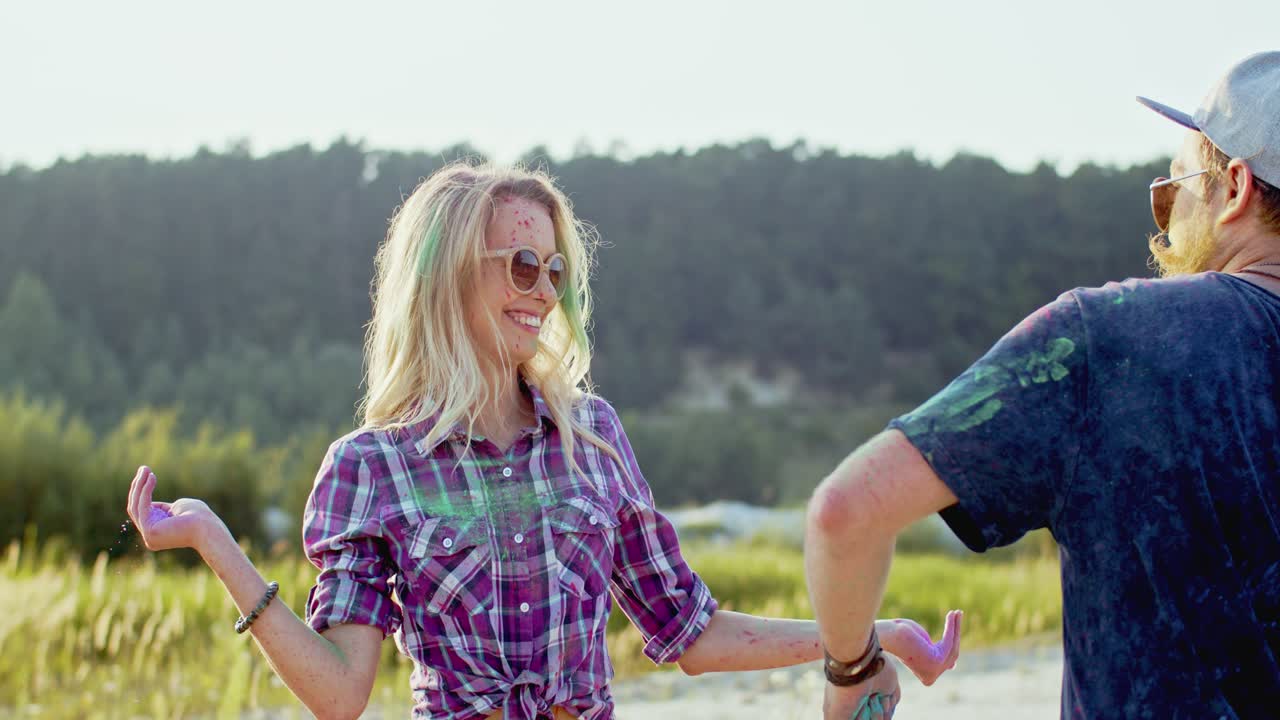 chico y chica alegres y elegantes divirtiéndose, riendo y tirando con pinturas coloridas al aire libre en la celebración holi