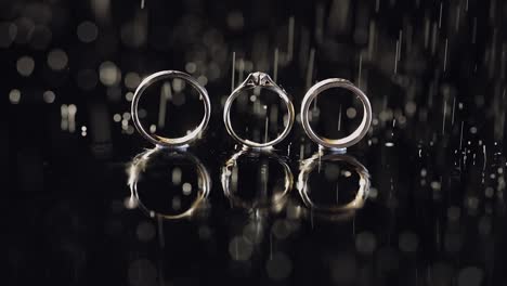 wedding and engagement rings lying on dark water surface shining with light