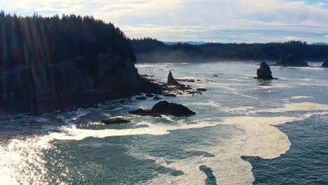 Stunning-tilting-up-aerial-drone-shot-of-the-gorgeous-Third-Beach-in-Forks,-Washington-with-large-rock-formations,-cliffs,-small-waves-and-sea-foam-on-a-warm-sunny-summer-morning