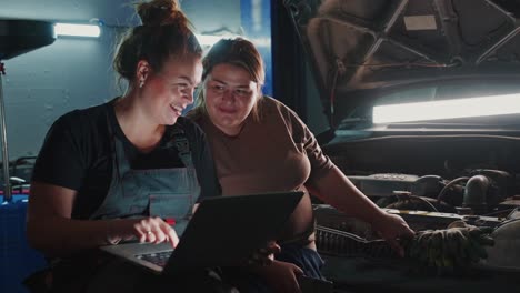 women mechanics inspecting car engine using laptop