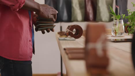 hands of african american craftsman arranging wallets on wooden surface in leather workshop