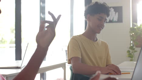 teenage boy in high school classroom writing in notebook, smiling and focusing