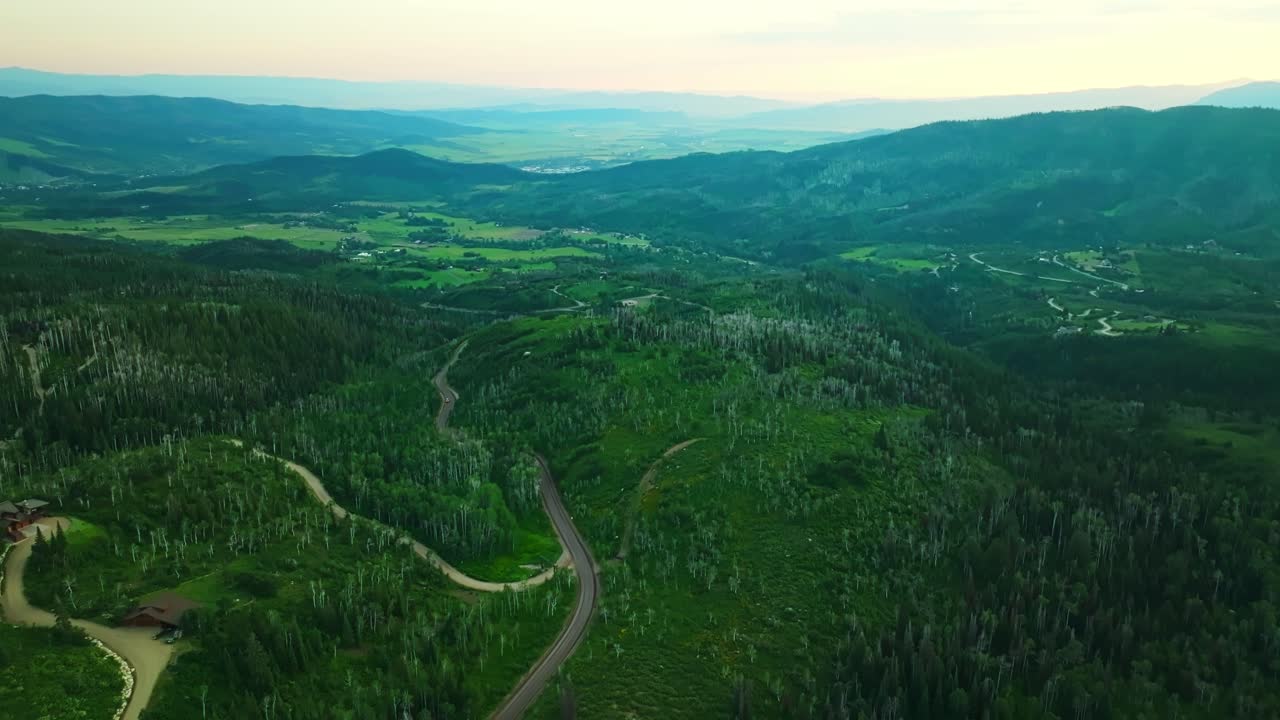 Aerial wide panoramic of winding road through hills at sunset in Steamboat Springs with golden tones and forest below